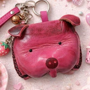 May include: A pink leather pig-shaped keychain with a strawberry charm, surrounded by other pink accessories. Includes a pink bracelet, a notebook, heart-shaped candies, and a plush bunny.
