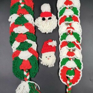 May include: Two long crocheted Christmas garlands featuring red, green, and white circular motifs with small metal bells, finished with yarn tassels. Between the garlands are two small crocheted Santa Claus faces with white beards.
