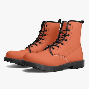 May include: A pair of ankle-high boots in a solid matte orange colour. These boots feature black laces, black metal eyelets, black trim along the collar and tongue, and a thick black rubber sole with a treaded bottom for traction and stability.