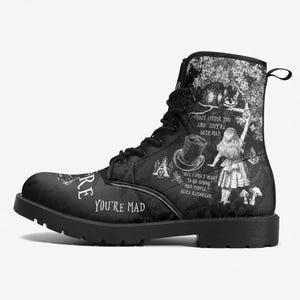 Könnte beinhalten: Ein schwarzer Schnürstiefel mit einem monochromen Grafikdruck, der von Alice im Wunderland inspiriert ist. Das Design zeigt Illustrationen von Alice, einem Zylinder und einer Katze sowie den Text "Visit either you like: they're both mad."