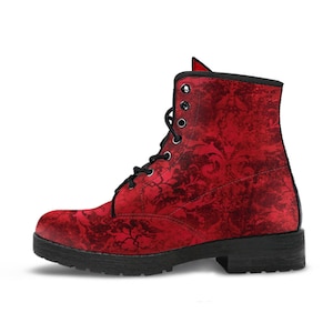 May include: A red combat boot with a black sole and laces. The boot features a dark floral pattern over a red background. The boot has a rounded toe and a short heel. The laces are black and go through black metal eyelets.