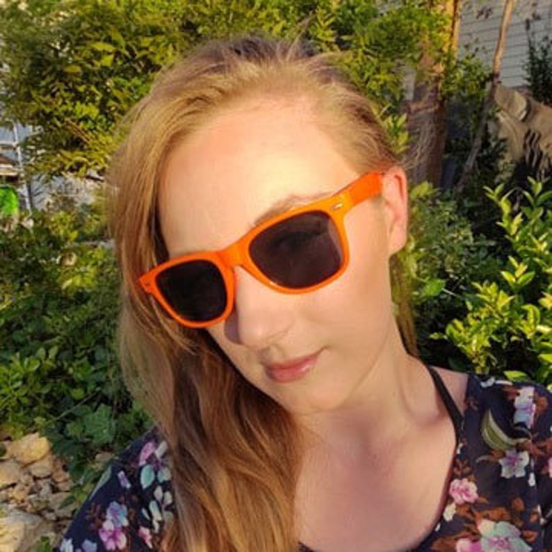 May include: A woman wearing orange sunglasses with dark lenses. The sunglasses have a square frame.