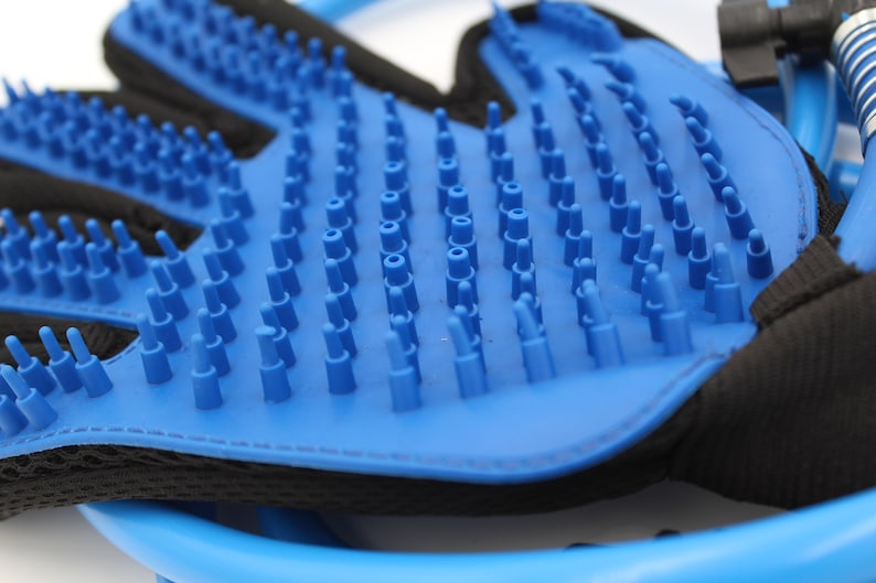 May include: A blue pet grooming glove with numerous soft, rounded bristles. The glove has a black mesh backing and a blue plastic frame. The bristles are designed to gently remove loose hair and massage the pet's skin.