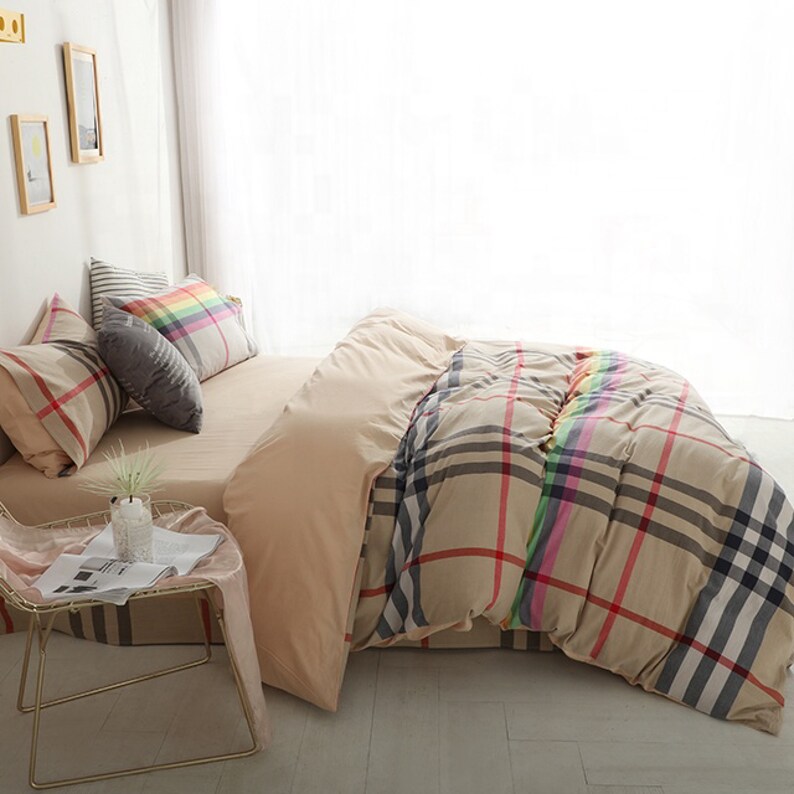 May include: Beige and white plaid bedding set with a rainbow stripe detail. The set includes a duvet cover, two pillowcases, and a decorative pillow.