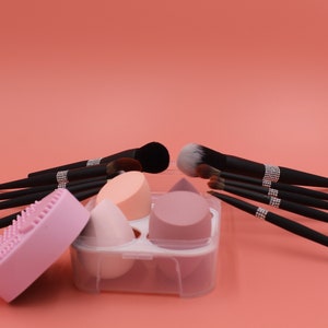 Puede incluir: Un conjunto de pinceles de maquillaje negros con detalles de pedrer&iacute;a, un limpiador de esponjas de maquillaje de silicona rosa y un estuche de pl&aacute;stico transparente con tres esponjas de maquillaje rosas y melocot&oacute;n.