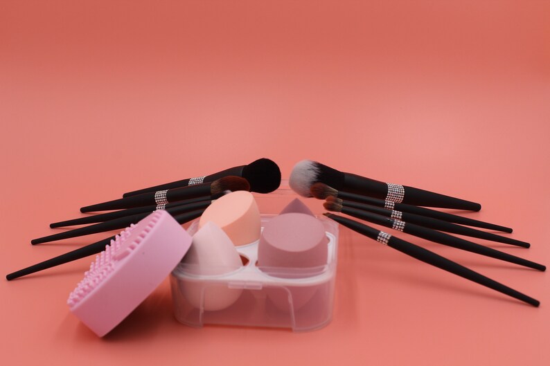 Puede incluir: Un conjunto de pinceles de maquillaje negros con detalles de pedrer&iacute;a, un limpiador de esponjas de maquillaje de silicona rosa y un estuche de pl&aacute;stico transparente con tres esponjas de maquillaje rosas y melocot&oacute;n.