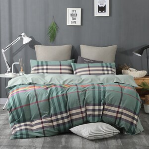 May include: A green and white plaid duvet cover with a colorful stripe detail. The duvet cover is on a bed with two pillows, one with a plaid pattern and the other with a solid color. The bed is in a bedroom with a gray wall and a lamp on a side table.