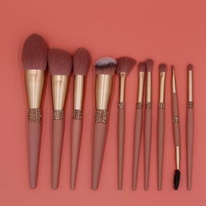Puede incluir: Conjunto de diez pinceles de maquillaje rosa y dorado con un detalle de pedrer&iacute;a en los mangos. Los pinceles tienen diferentes formas y tama&ntilde;os para diversas aplicaciones de maquillaje.