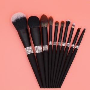 Puede incluir: Un conjunto de 10 pinceles de maquillaje negros con detalles de pedrer&iacute;a. Los pinceles tienen diferentes formas y tama&ntilde;os para diversas aplicaciones de maquillaje.