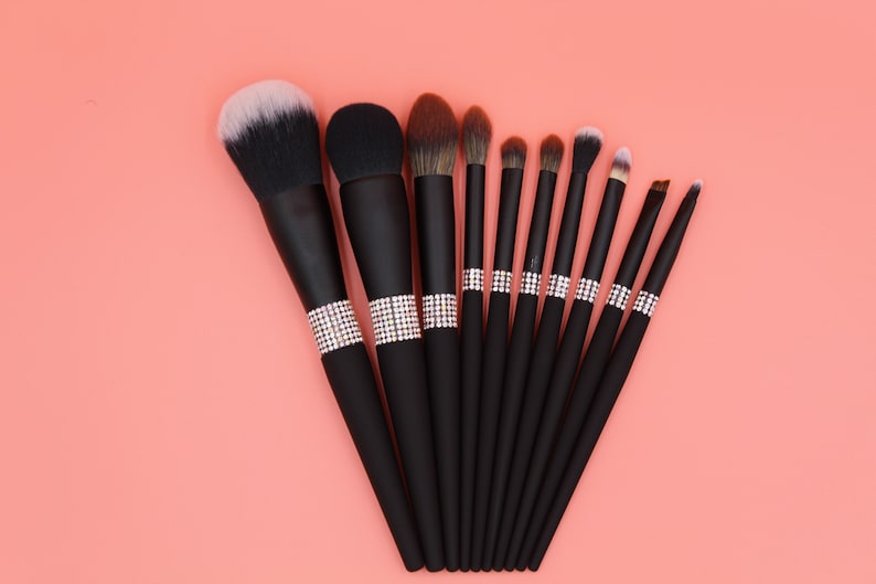 Puede incluir: Un conjunto de 10 pinceles de maquillaje negros con detalles de pedrer&iacute;a. Los pinceles tienen diferentes formas y tama&ntilde;os para diversas aplicaciones de maquillaje.