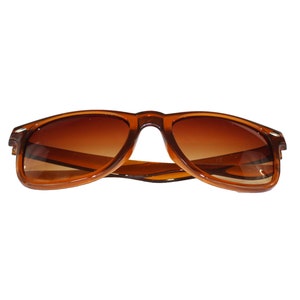 May include: Brown plastic sunglasses with brown lenses. The sunglasses are in focus and the background is blurred.