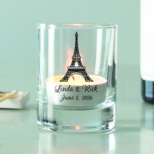 May include: A clear glass votive candle holder with a black and white Eiffel Tower design and the text "Linda & Rick June 8, 2026".