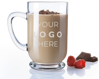 Könnte beinhalten: Eine klare Glas-Tasse mit Henkel, gefüllt mit einem hellbraunen Getränk. Die Tasse hat den Text "YOUR LOGO HERE" auf der Seite graviert. Auf einer weißen Oberfläche liegen drei rote Himbeeren und zwei Stücke dunkle Schokolade.
