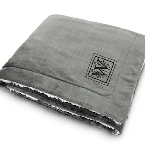 May include: A gray fleece blanket with a white sherpa lining. The blanket has a monogrammed initial "W" in a decorative frame.