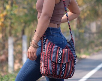 Può includere: Una borsa a tracolla con un design colorato e fantasia. La borsa ha una chiusura con patta e una lunga tracolla. Il motivo include strisce rosse, nere e bianche e forme geometriche. La borsa è portata a spalla.