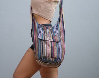 May include: A woman wearing a brown tank top and denim shorts carries a colorful striped shoulder bag with a large pocket. The bag is made of woven fabric and has a long strap.