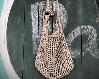 May include: A beige crocheted net bag hanging on a green wooden door with white paint. The bag has a wooden ring at the top.