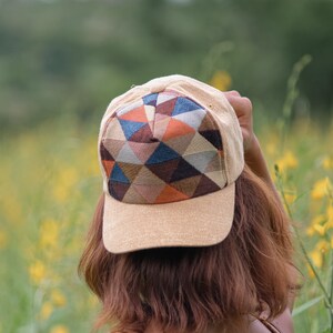 Puede incluir: Una gorra de béisbol beige con un patrón geométrico en tonos de marrón, naranja, azul y gris. La gorra tiene una visera curvada y una parte superior plana.