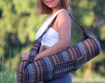May include: A woman is holding a colorful yoga mat bag with a long strap. The bag has a geometric pattern in shades of brown, red, blue, and white.