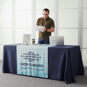 May include: A navy blue tablecloth with a white table runner featuring a blue and white graphic design of a globe with circuit board lines and the text "LAWSON TECHNOLOGIES Providing the IT connection you need".