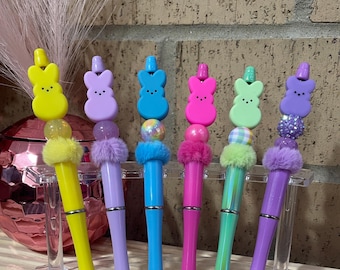 Peut inclure: Six stylos colorés avec des chapeaux en forme de lapin et des pompons moelleux. Les stylos sont disposés dans un porte-stylos en plastique transparent.