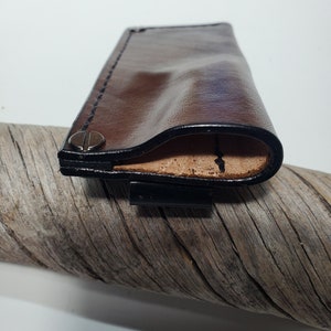 May include: A brown leather case with black stitching detail and a metal snap closure. The case is folded open to reveal a tan leather interior.