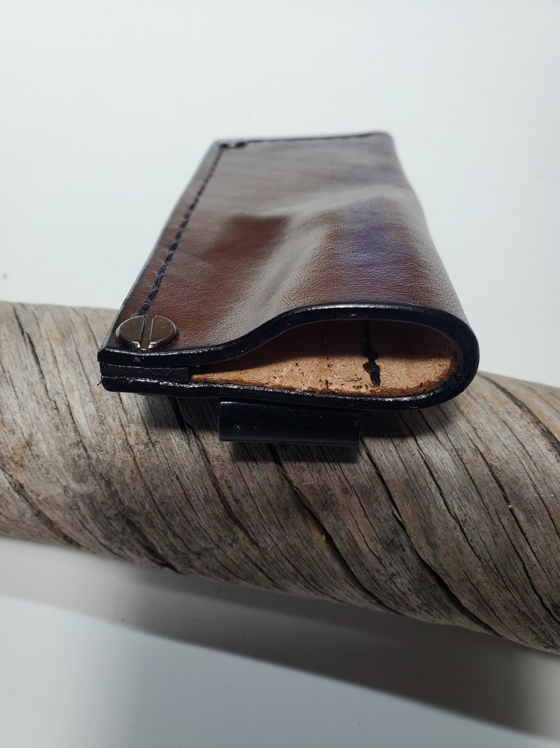 May include: A brown leather case with black stitching detail and a metal snap closure. The case is folded open to reveal a tan leather interior.