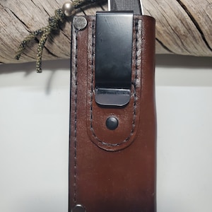 May include: A brown leather knife sheath with a black metal clip and a silver bead on the lanyard.