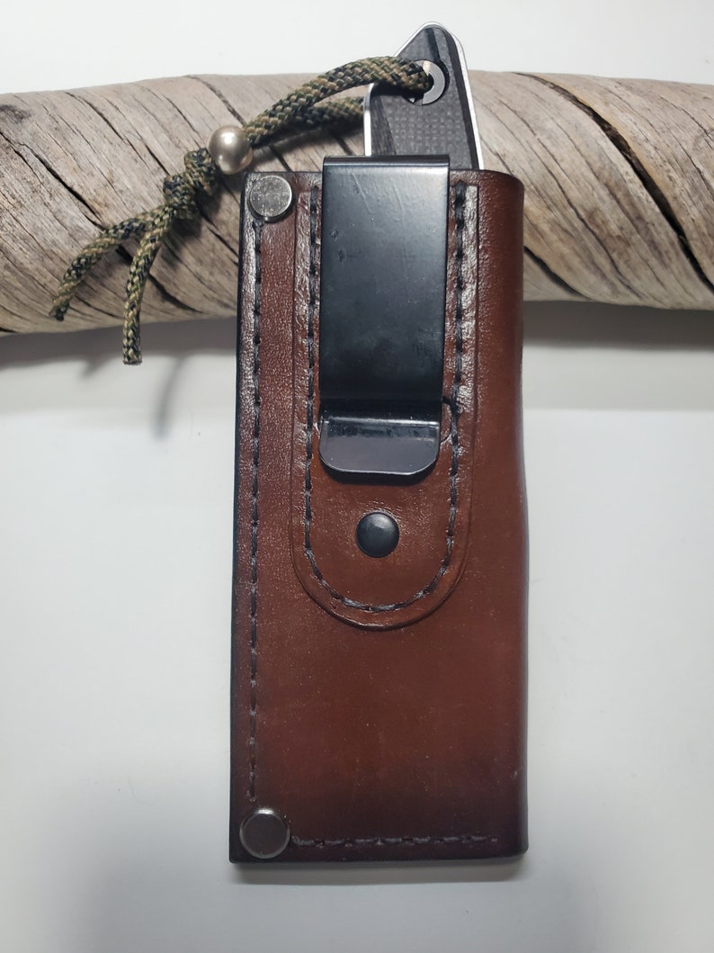 May include: A brown leather knife sheath with a black metal clip and a silver bead on the lanyard.