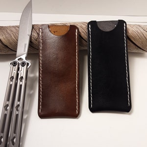 May include: Two leather knife sheaths, one brown and one black, with white stitching. The sheaths are made of a high-quality leather and have a simple, elegant design.