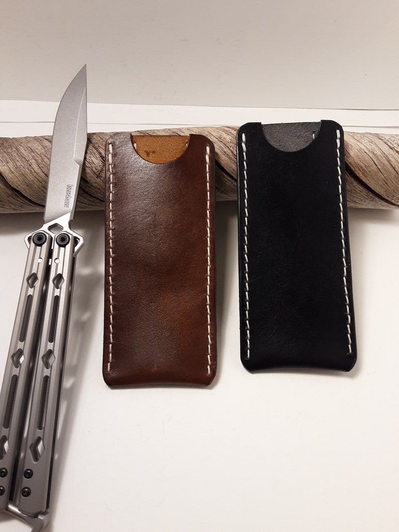 May include: Two leather knife sheaths, one brown and one black, with white stitching. The sheaths are made of a high-quality leather and have a simple, elegant design.