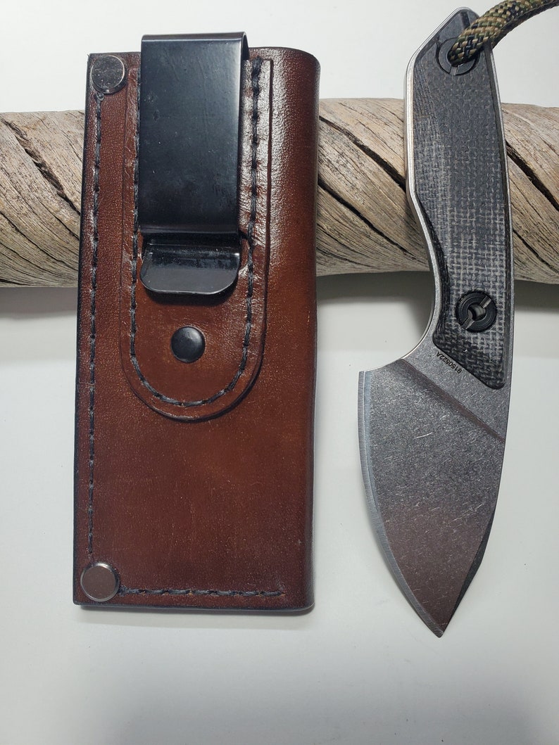 May include: A brown leather knife sheath with a belt clip and a silver knife with a black and grey handle.