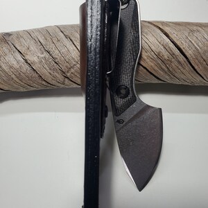 May include: A black leather knife sheath with a carbon fibre pocket knife with a black blade. The knife is attached to a green and brown lanyard.