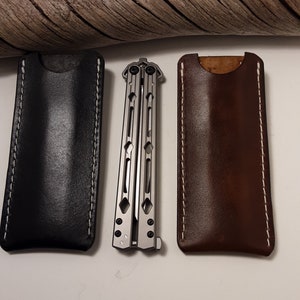 May include: Two leather sheaths for a butterfly knife, one black and one brown, with white stitching. The knife is made of metal and has a silver finish.
