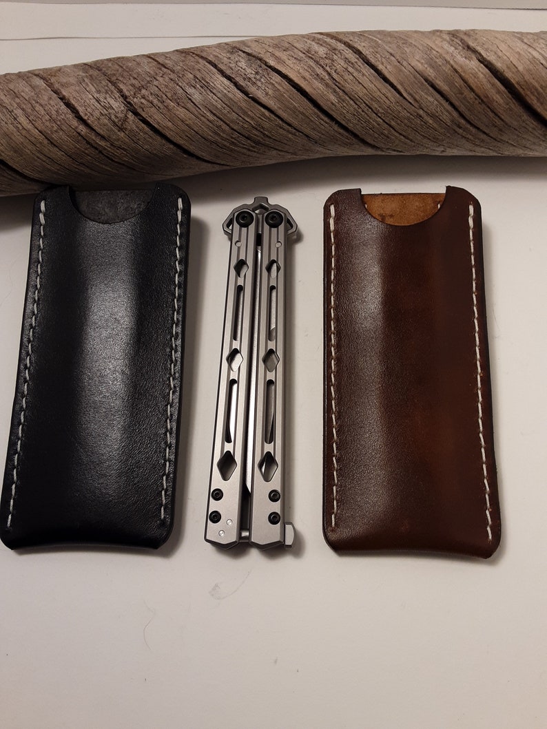May include: Two leather sheaths for a butterfly knife, one black and one brown, with white stitching. The knife is made of metal and has a silver finish.
