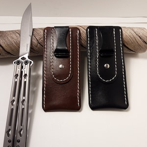 May include: Two leather knife sheaths with a black clip and white stitching. One sheath is brown and the other is black. A silver butterfly knife is shown on the left side of the image.