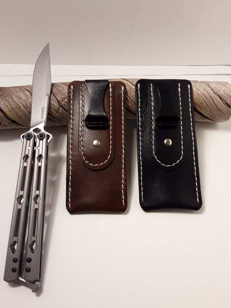 May include: Two leather knife sheaths with a black clip and white stitching. One sheath is brown and the other is black. A silver butterfly knife is shown on the left side of the image.