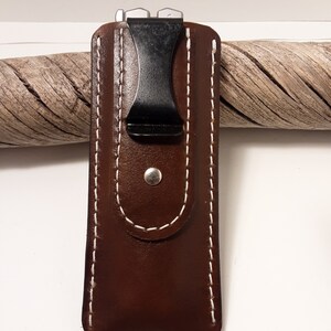 May include: A brown leather case with white stitching and a black clip. The case is designed to hold a small pocket knife or multi-tool.