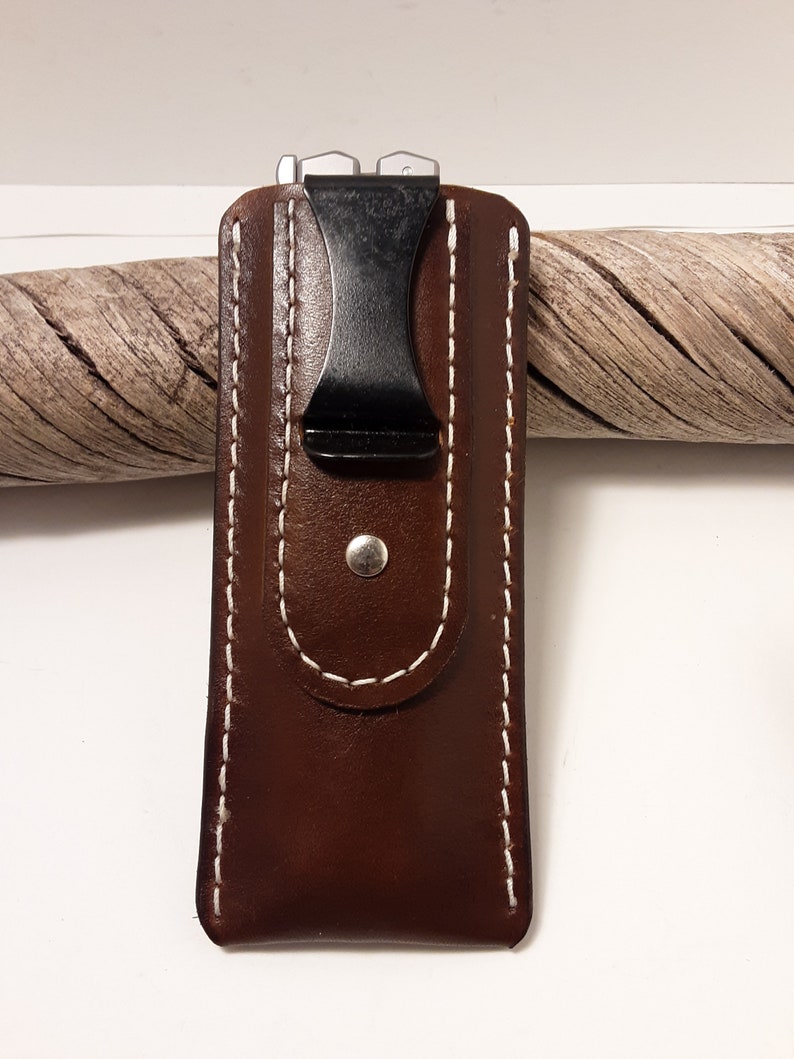 May include: A brown leather case with white stitching and a black clip. The case is designed to hold a small pocket knife or multi-tool.
