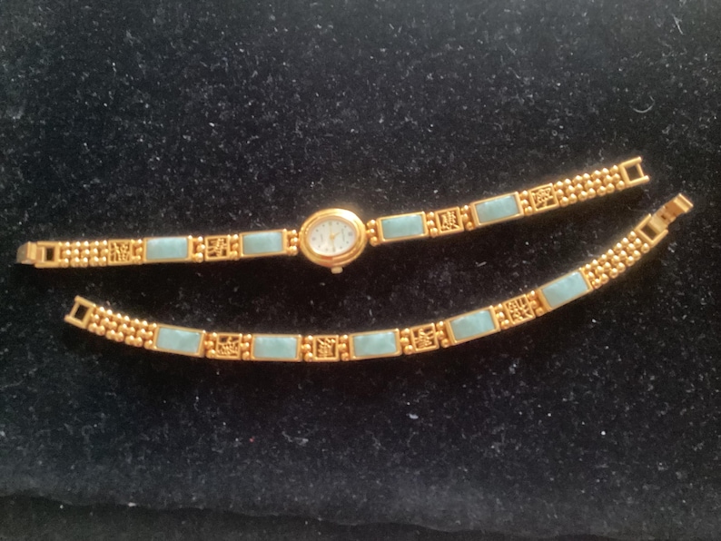 May include: Gold-toned wristwatch with a light blue rectangular band and a small oval face. The watch band is separated into two pieces, displaying the intricate design and the watch's delicate features.