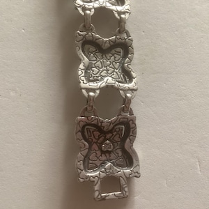 May include: Silver bracelet with a repeating pattern of interlocking hearts. The bracelet is made of metal and has a polished finish.