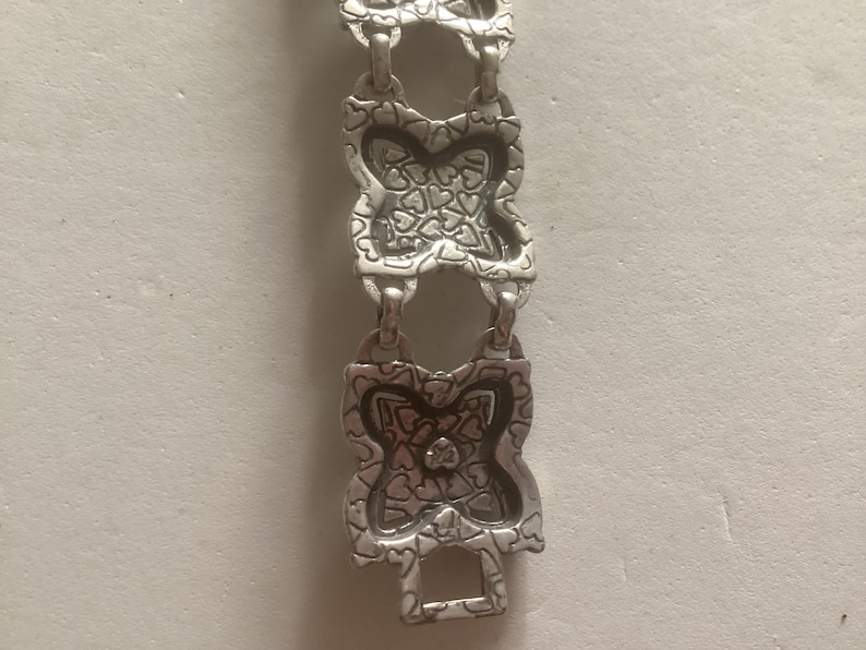 May include: Silver bracelet with a repeating pattern of interlocking hearts. The bracelet is made of metal and has a polished finish.