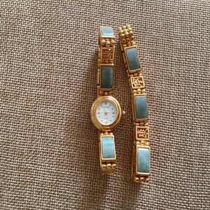 May include: A gold-toned watch and bracelet set with rectangular, light blue-green stones. The watch has a white face with gold hands and hour markers. The bracelet has a similar design, with gold links and matching stones.