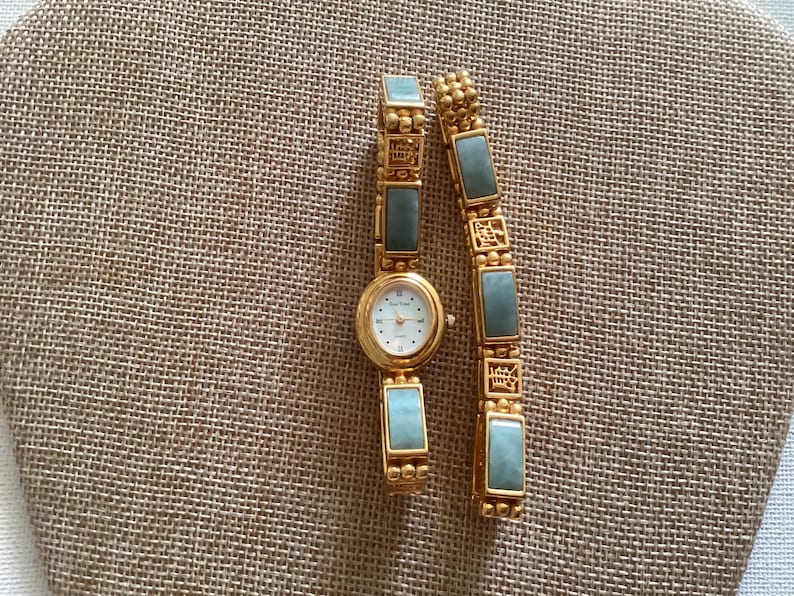 May include: A gold-toned watch and bracelet set with rectangular, light blue-green stones. The watch has a white face with gold hands and hour markers. The bracelet has a similar design, with gold links and matching stones.