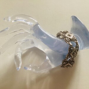 May include: Silver bracelet with a geometric design. The bracelet is made of multiple linked pieces with a square shape in the center of each piece.