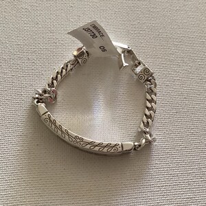 K&ouml;nnte beinhalten: Ein silbernes Armband mit einem Panzerketten-Design. Das Armband hat einen dekorativen Stab mit einem eingravierten Blattmuster. Ein Etikett ist am Armband befestigt mit dem Wort "EMBRACE" und der Nummer "J37730".