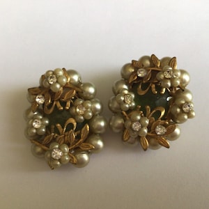 Può includere: Un paio di orecchini vintage a clip con un centro in vetro verde circondato da perle finte e strass. Gli orecchini sono dorati e hanno un design floreale.