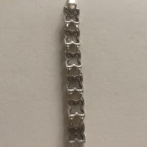 May include: A silver bracelet with a butterfly design. The bracelet is made of metal and has a polished finish.