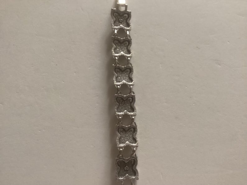 May include: A silver bracelet with a butterfly design. The bracelet is made of metal and has a polished finish.