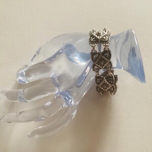 May include: Silver bracelet with a chain link design and intricate square-shaped charms. The charms have a floral pattern and are connected by a delicate chain.